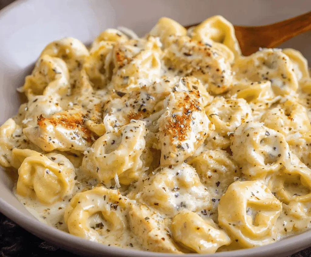 Creamy Garlic Parmesan Chicken Tortellini served with fresh herbs and grated cheese on a white plate, featuring tender tortellini pasta with flavorful chicken and a rich garlic Parmesan sauce.