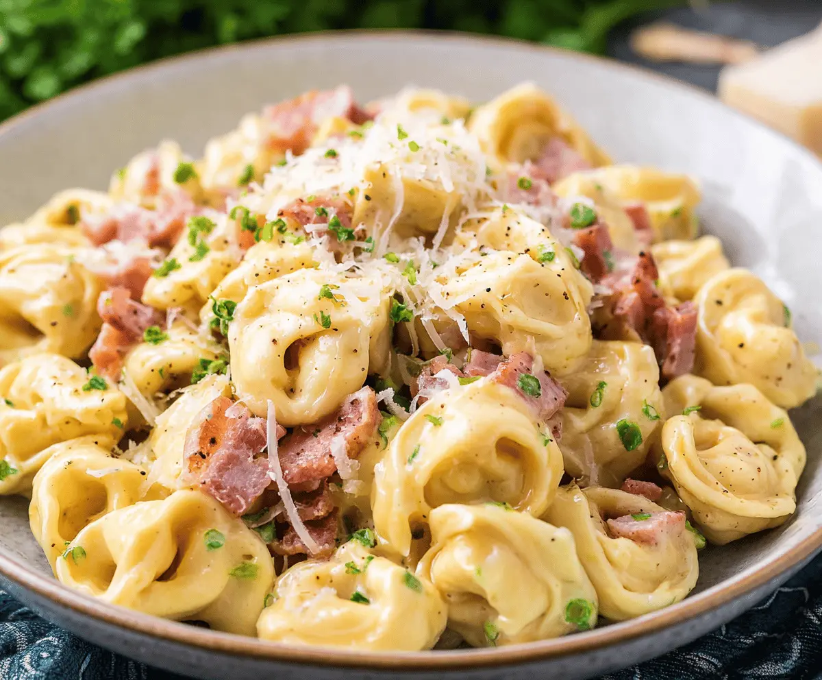 Creamy tortellini carbonara in a white bowl garnished with chopped herbs and grated cheese, served on a rustic wooden table.